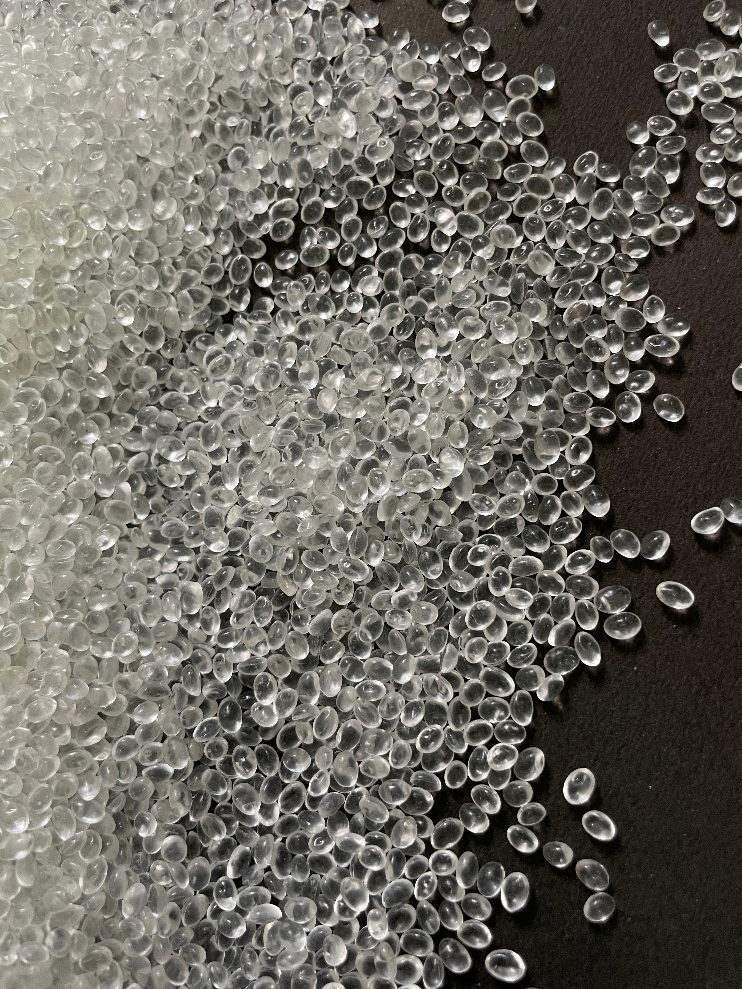 Clear bioplastic granules spread on a dark surface